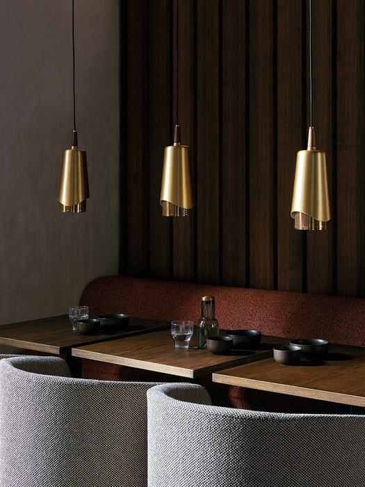 Three brass and walnut Umanoff Pendants hang over wooden tables in a sophisticated, dimly lit restaurant setting.