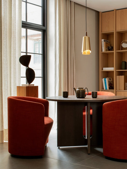 The brass Umanoff Pendant hangs over the dark wood Androgyne Dining Table and orange Tearoom chairs in a dining room.