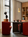 The brass Umanoff Pendant hangs over the dark wood Androgyne Dining Table and orange Tearoom chairs in a dining room.