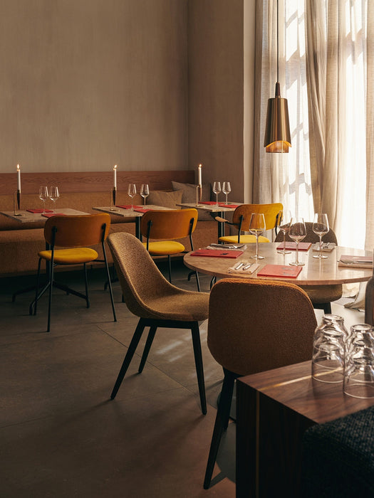 The brass Umanoff Pendant light hanging over a set dining table in an elegant, warmly lit restaurant with mustard chairs.