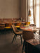 The brass Umanoff Pendant light hanging over a set dining table in an elegant, warmly lit restaurant with mustard chairs.