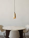 The Umanoff Pendant in brass and walnut hangs illuminated over a round marble dining table with three light-coloured chairs.
