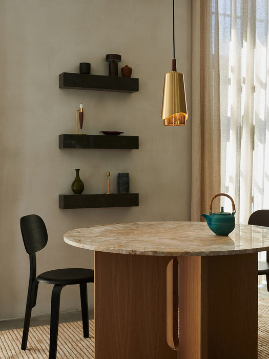 The Umanoff Pendant light in brass hangs above the marble Androgyne Dining Table. A black Afteroom chair sits beside it.