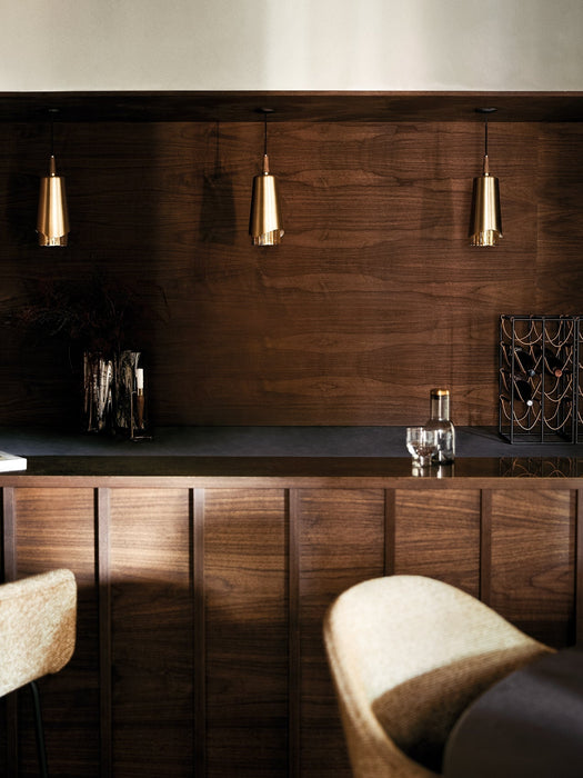 Three brass Umanoff Pendants hang over a dark wood bar counter. On the counter is a wine rack, vase and glassware.