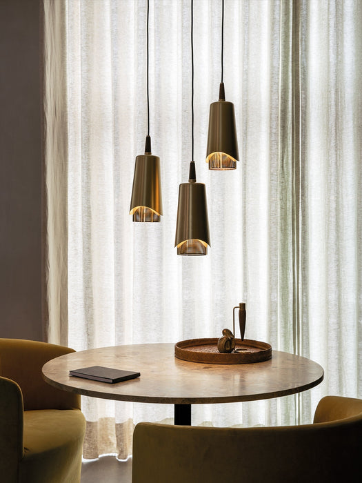 Three lit Umanoff Pendants in brass hang over a round dining table with mustard yellow chairs in front of sheer curtains.
