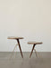 Two Umanoff Side Tables, in different heights, with dark walnut tops and brass tripod legs, against an off-white wall.