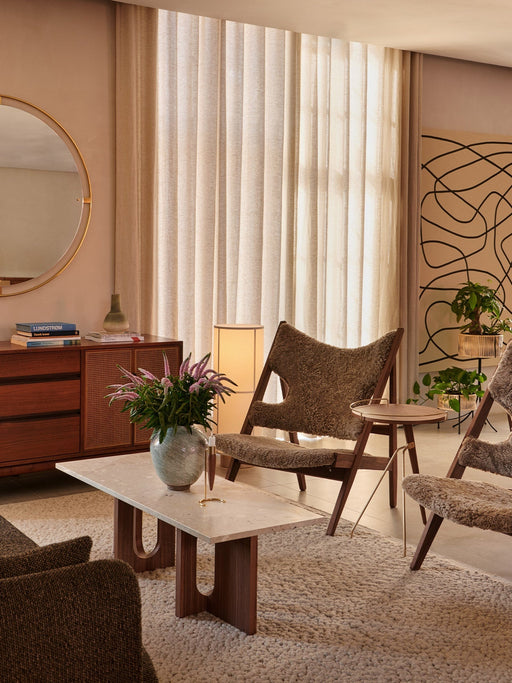 Side view of the Umanoff Side Table in a living room next to a shearling armchair. Marble coffee table in the foreground.