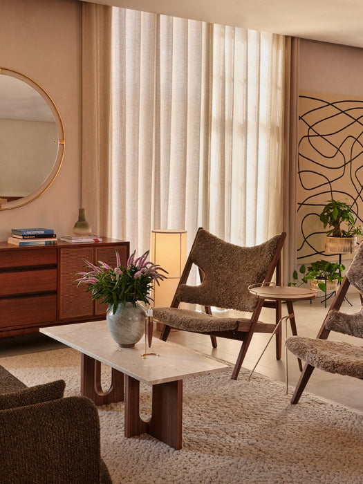 Side view of the Umanoff Side Table in a living room next to a shearling armchair. Marble coffee table in the foreground.