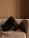 A person in dark trousers and a brown jumper relaxing on the light-coloured, textured Vilhelm Sofa against a warm brown wall.