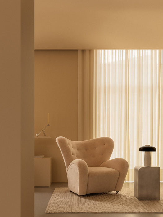 A tranquil, beige-toned room with The Tired Man armchair next to the Volume Side Table holding a Reverse Table Lamp.