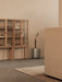 A silver Volume Side Table holding a black vase in a neutral-toned room with a Curiosity Cabinet and beige Tearoom Sofa.