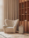The Volume Side Table in a cozy room, next to a cream boucle Tired Man armchair, with a wooden Curiosity Cabinet in the back.