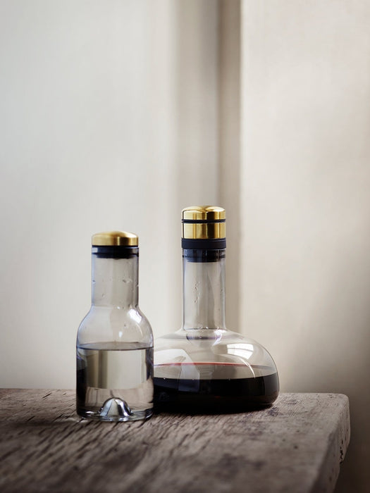 A large glass Menu Wine Breather Carafe filled with red wine sits next to a smaller matching water carafe on a wood surface.