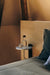 The marble Corbel Shelf by Audo CPH used as a bedside table, holding a glass water bottle and tumbler next to a bed.