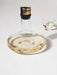 The Audo Wine Breather Deluxe, a wide glass carafe with gold stopper, filled with white wine next to a small drinking glass.