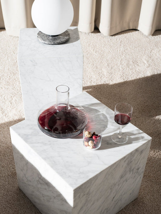 A Winebreather decanter with red wine sits on a marble Plinth next to a TR Bulb lamp on a taller Plinth in a living space.