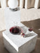 A Winebreather decanter with red wine sits on a marble Plinth next to a TR Bulb lamp on a taller Plinth in a living space.