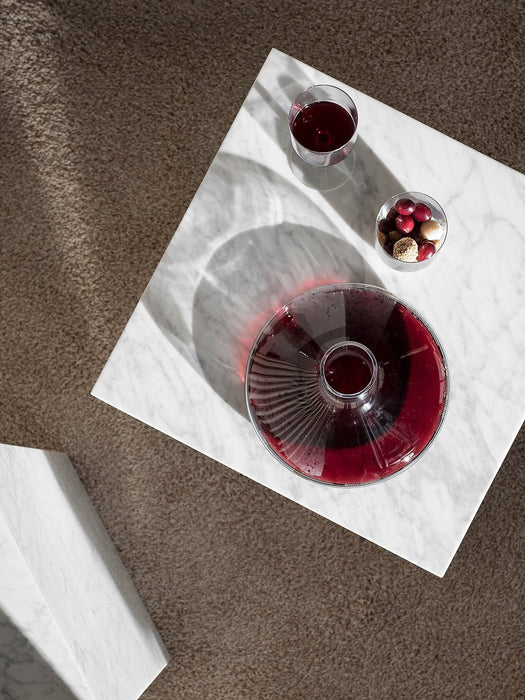 Overhead view of a glass Winebreather carafe and a glass of red wine on a white marble Plinth table next to a bowl of snacks.
