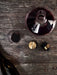 A flat lay of the Wine Breather Carafe with red wine, a glass, its brass stopper, and a bottle on a dark wood table.