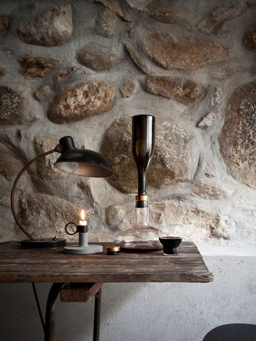 The Wine Breather Carafe on a rustic wooden table against a stone wall, beside a lit candle, lamp, and glass of red wine.