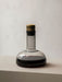 The Audo Wine Breather Carafe in smoked glass with a brass lid, sits on a grey surface, partially filled with red wine.