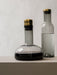 A Wine Breather Carafe of red wine and a Bottle Carafe of water, both in smoked glass with brass lids, on a light surface.