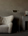 The polished aluminium Wing Floor Lamp stands in a living room beside a cream shearling armchair and a modern grey fireplace.