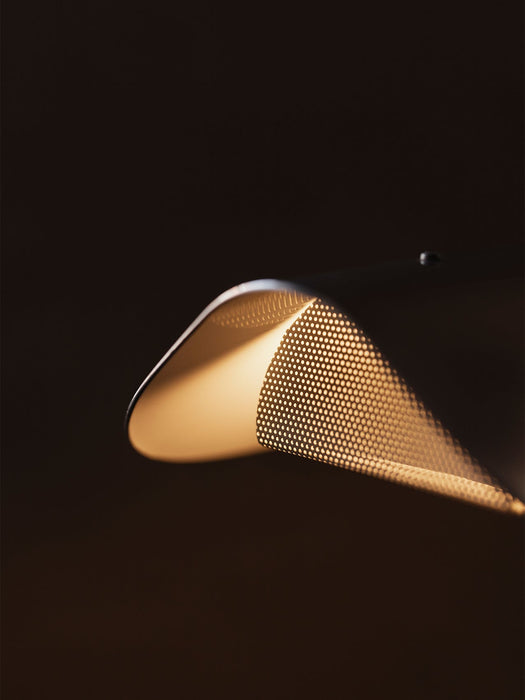Close-up of the Wing Table Lamp's polished aluminium shade, showing its perforated pattern and warm glow from within.