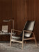 A polished aluminium Wing Table Lamp on a marble Plinth Bridge table illuminates a dark leather Seal High Back armchair.