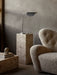 A polished aluminium Wing Table Lamp sits atop a marble Plinth, next to a cream-coloured, textured The Tired Man armchair.