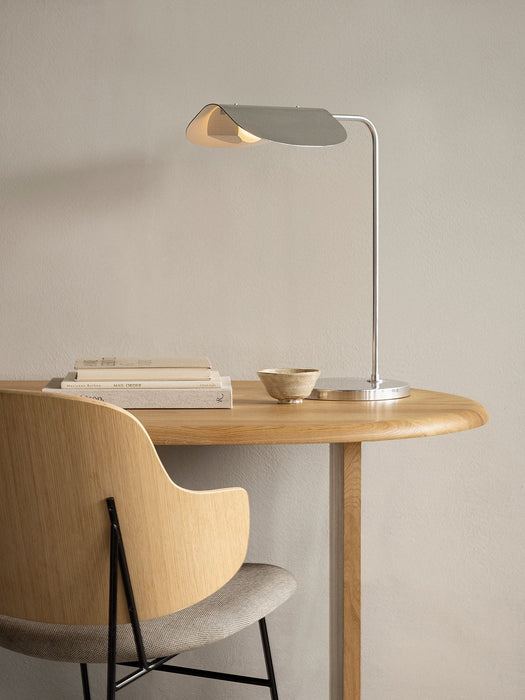 A sleek, polished aluminium Wing Table Lamp on a light oak Eclipse desk. Beside it are books, a bowl, and a Penguin chair.