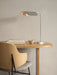 A sleek, polished aluminium Wing Table Lamp on a light oak Eclipse desk. Beside it are books, a bowl, and a Penguin chair.