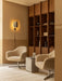 A lounge with a Wing Wall Lamp, two Harbour Lounge Chairs, a Volume Side Table, Tile Rug, and a wooden bookcase.