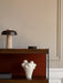 Close-up of a dark wood shelving unit styled with a travertine lamp, coasters, a white abstract vase, and an Audo box.