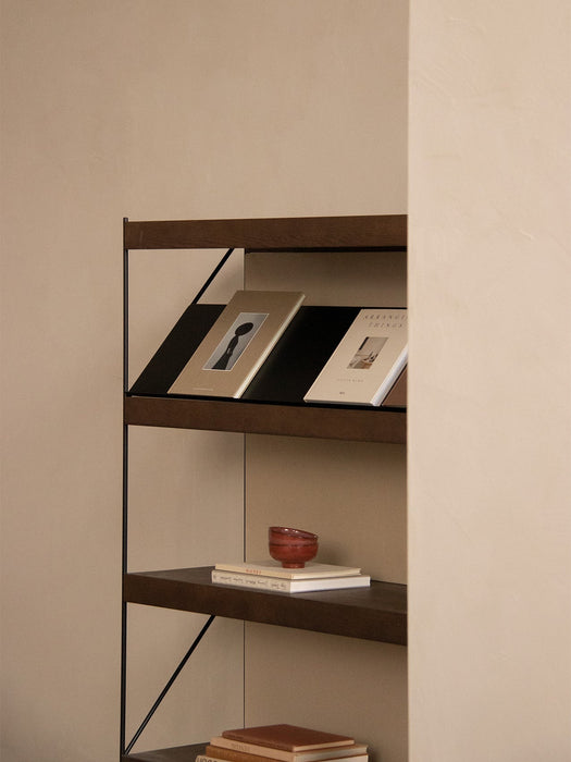 A close-up of the dark oak Zet Storage System with a black frame, styled with books and a small bowl against a neutral wall.
