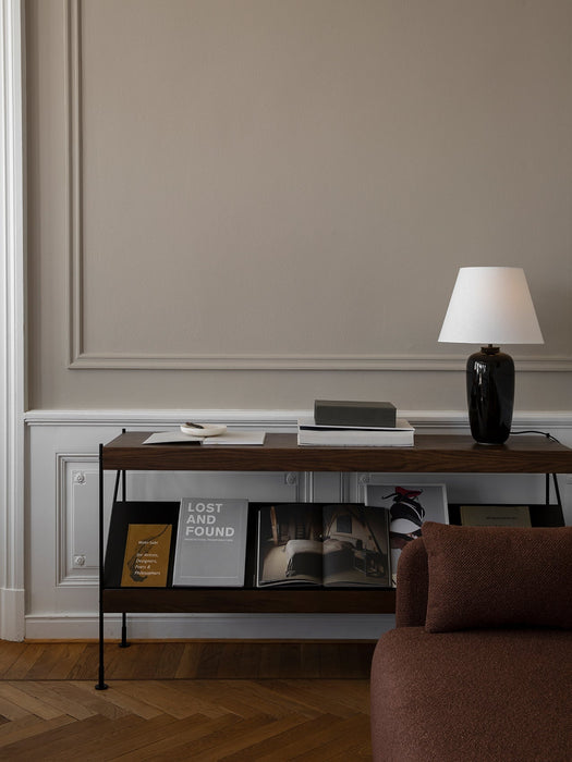 A Zet Storage System in dark oak wood, styled with books and a black lamp, sits against a taupe wall with white panelling.