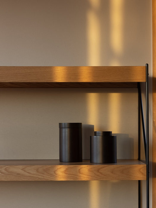 A close-up of the Zet Storage System's oak shelves and black frame. Two black containers sit on a shelf in warm sunlight.