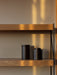 A close-up of the Zet Storage System's oak shelves and black frame. Two black containers sit on a shelf in warm sunlight.