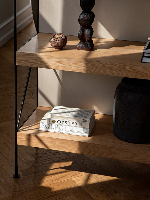 Sunlit close-up of the Zet Storage System's oak shelves and black frame, styled with books, a vase, and decorative objects.