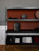 A close-up of the black Zet Storage System, styled with rustic vases and books against a terracotta back panel.