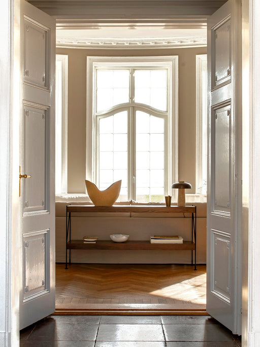 A view through open white doors of the Zet Storage System in dark oak, placed under a large, bright window in a classic room.