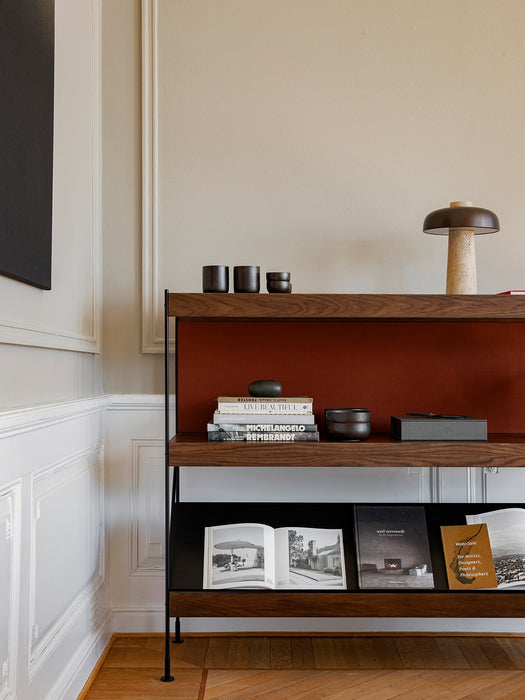 A detailed view of the dark wood Zet Storage System, styled with art books, ceramics, and a table lamp in a classic interior.