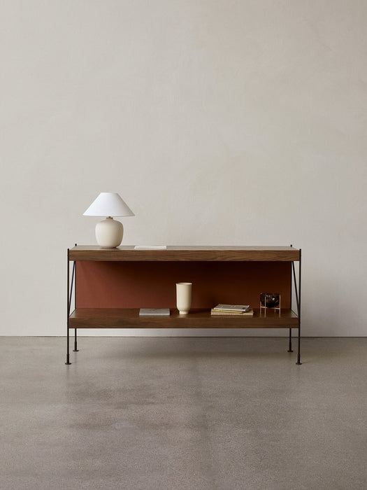 A dark wood Zet Storage System with a black frame, styled with a cream lamp, books, and a vase against a light grey wall.