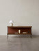 A dark wood Zet Storage System with a black frame, styled with a cream lamp, books, and a vase against a light grey wall.