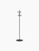 A tall, minimalist black coat stand with a slim pole, flat circular base, and two sets of cross-shaped hooks.
