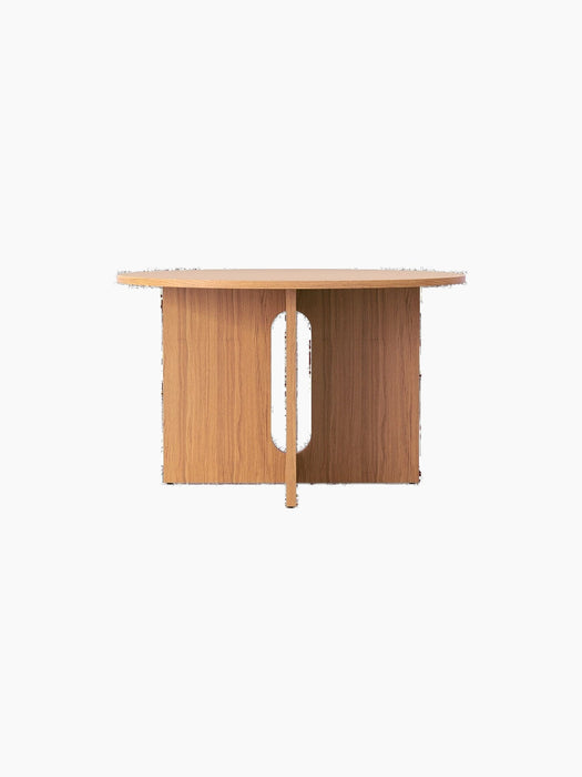 A front view of the round Androgyne Dining Table in natural oak, featuring a wide base with a central, oblong cutout.