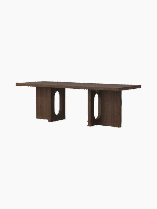 Angled view of the Androgyne Lounge Table in dark stained oak, with two wide legs featuring distinctive oval cutouts.