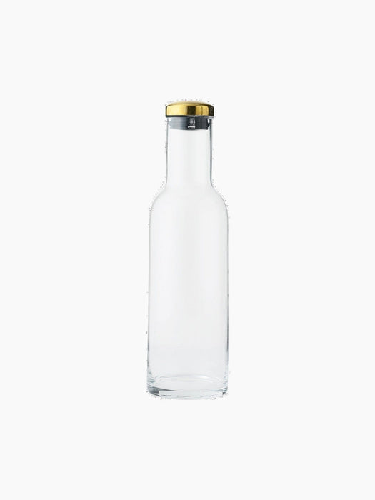 A minimalist clear glass Bottle Carafe with a straight body and sloped shoulders, sealed with a polished brass and black lid.