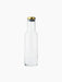 A minimalist clear glass Bottle Carafe with a straight body and sloped shoulders, sealed with a polished brass and black lid.