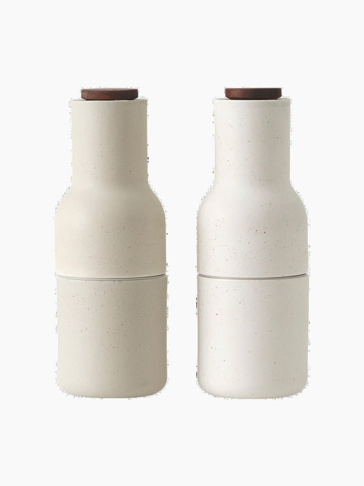 A pair of Bottle Grinders in a sand-coloured ceramic with a speckled finish and a dark wood lid, on a plain black background.
